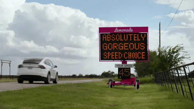 Lemonade's pink Slow Sign displaying a safe-driving message beside a road near Austin