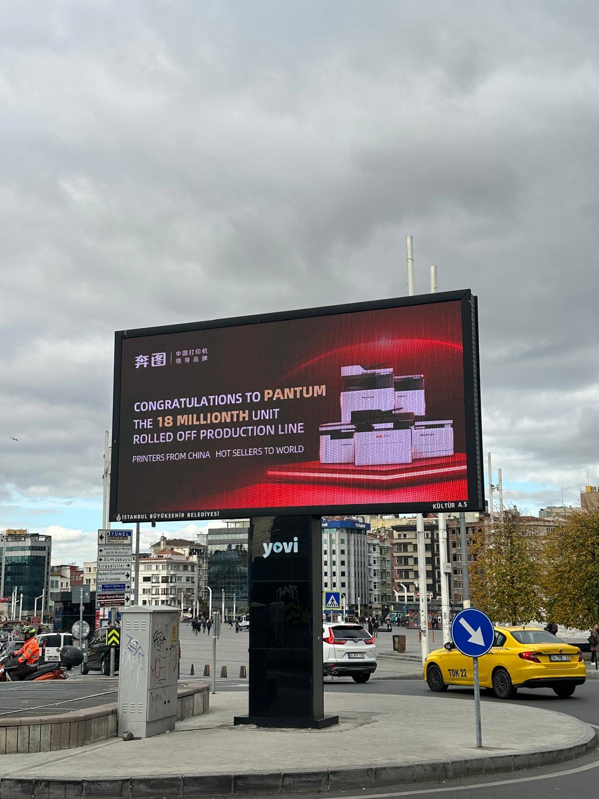 A landscape Yovi digital billboard displaying a Pantum campaign on the road edge of Taksim Square in Istanbul